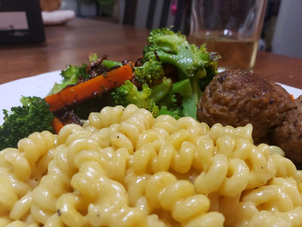 a diner plat of curly pasta, vegetables and some kind of meatballs