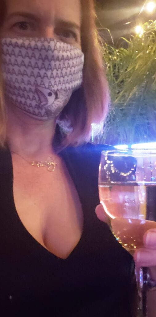 selfie of a person wearing a mask and a black dress holding a glass of wine