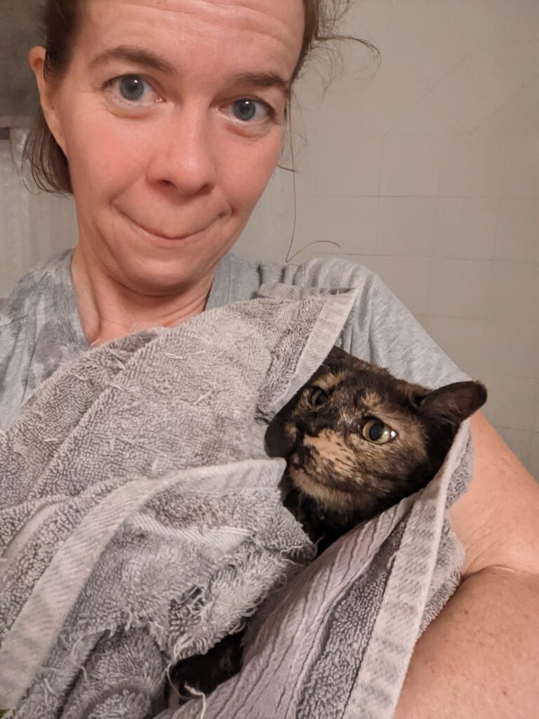 a person is making an nervous face while holding a cat wrapped in a towel