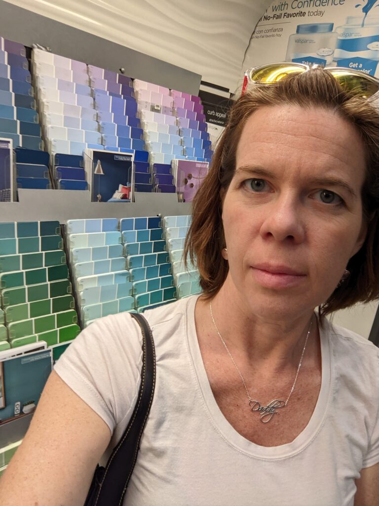 selfie of a tired looking person in a pain store next to paint samples