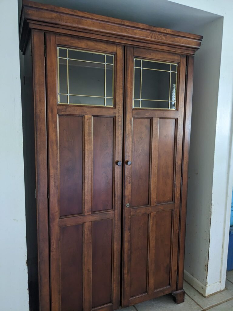 a tall cabinet made of dark wood with small windows at the top is in a small alcove