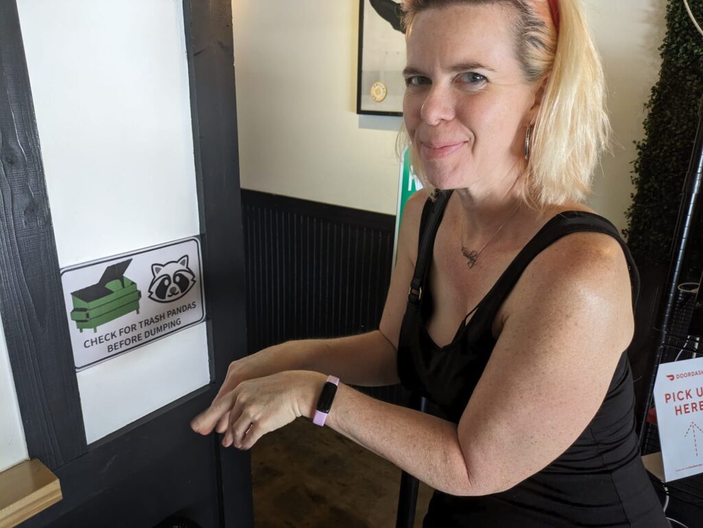a person is making a dramatic gesture next to a sign with a raccoon and a dumpster on it