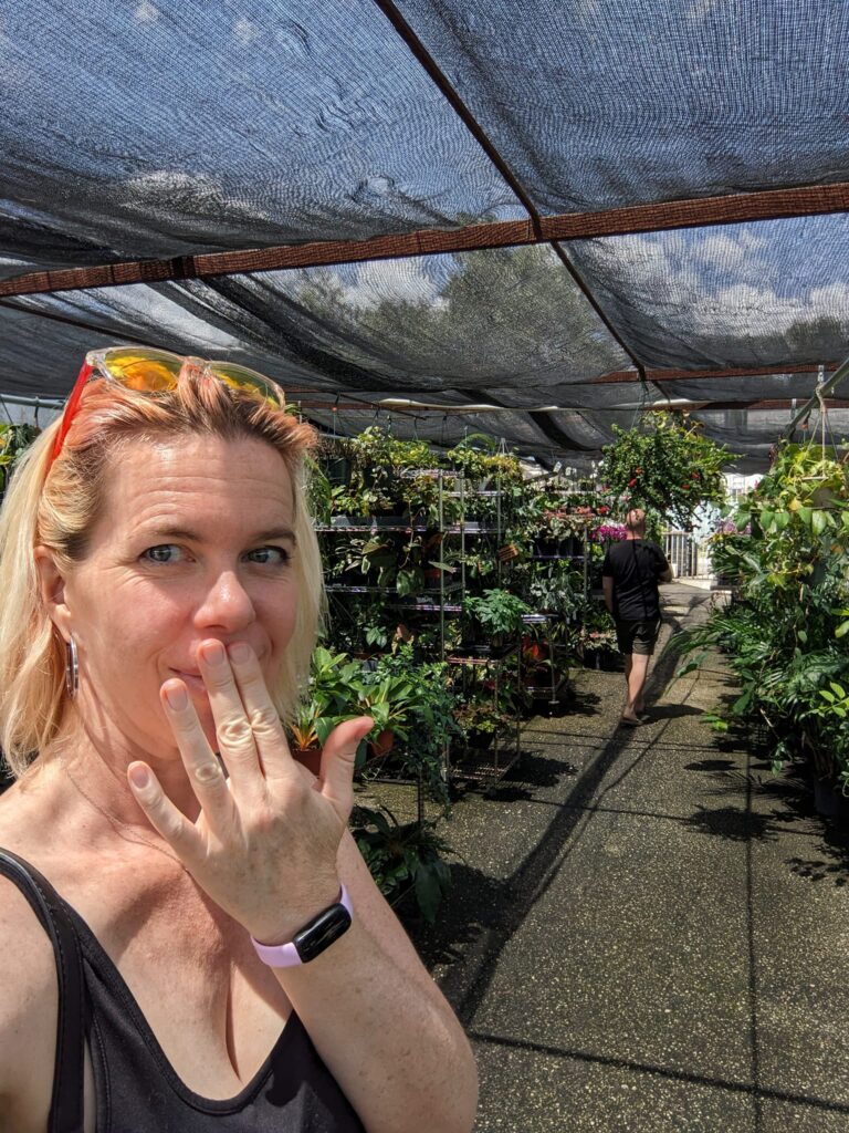 a person is making a face in an outdoors nursery with many plants under a fabric awning