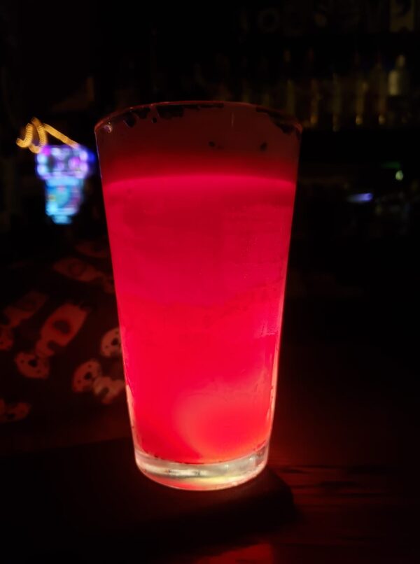 a pint glass of pink fluid is illuminated from below in a very dark space
