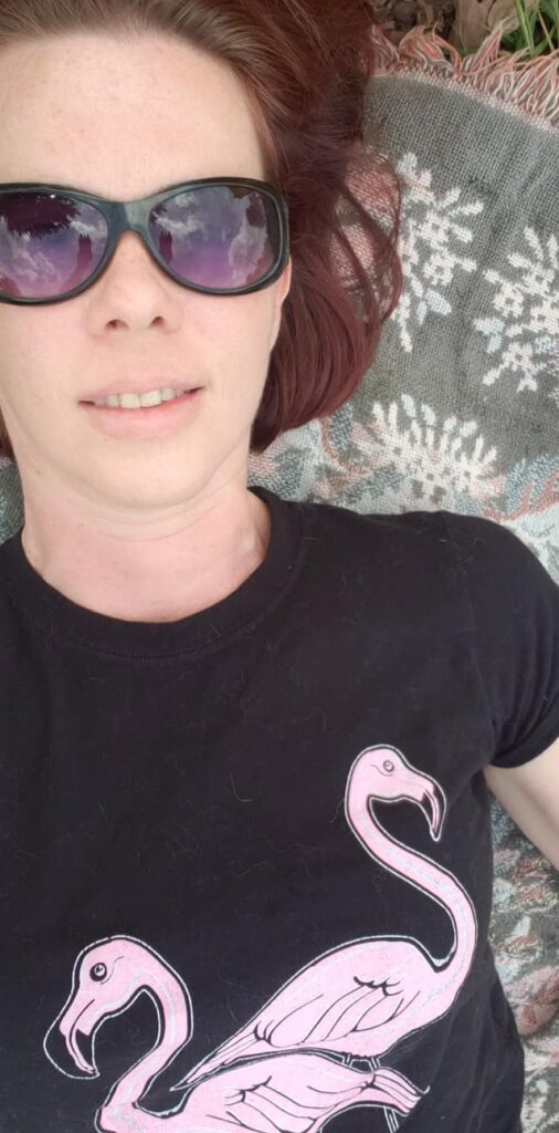 selfie of a person in big goggle sunglasses and a flamingo t-shirt laying back on a blanket
