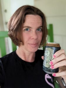 a person with short bobbed hair is sitting in a green chair and holding up a can of beer