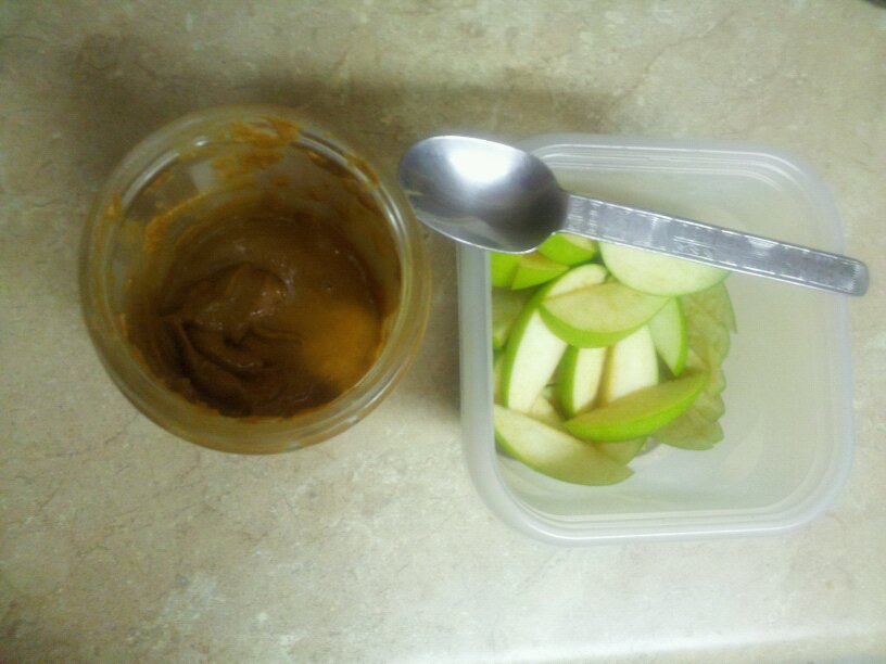 a jar of peanut butter and a bowl of sliced apples shown from above