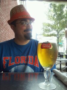 a man in an orange hat is smiling over a glass of beer