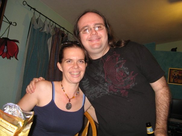 a seated person and standing person are hugging while smiling for a picture in shat looks like a living room