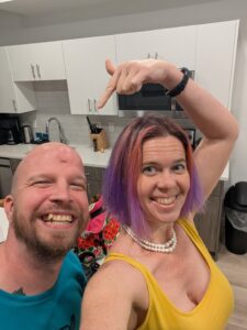 selfie of two people smiling in a kitchen with one person pointing at the counter in the background