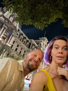 two people are taking a blurry selfie with a very large elaborate building against a night sky