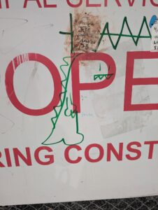 a sign that has OPE is graffitied to include a dinosaur with the P as its face