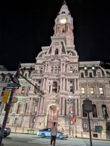 a very large elaborate building with a tall tower in the center is lit from the front against a dark night sky