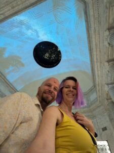 two people are taking a selfie angled up to show the vaulted curved ceiling above them lit with a blue light