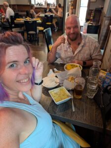 selfie of two people on either side of a small dinner table in an India restaurant with many dishes between them