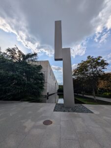 a large metal sculpture in front of a reflecting pool looks like a simplified lightning bolt