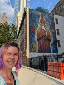a person is smiling with a mural of a person holding their hands up to cup the roots of a tree in the background