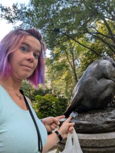 a person is looking mock surprised and pointing at the back side of a bronze lion statue