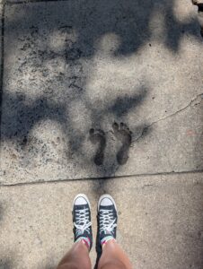 a pair of feet have stopped on a sidewalk next to two feet impressions in cement