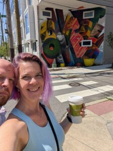 two people have stopped in front of a building with a chaotic mural of letters in many colors and patterns