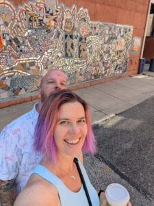 two people are standing in front of a wall covered in eclectic tile mosaic