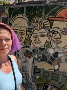 a selfie of a person standing in front of a wall with a tiled mosaic showing three stylized faces