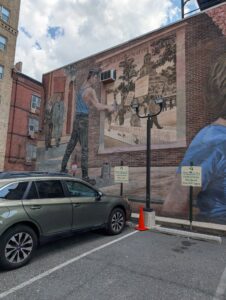 the side of an urban brick building has a mural of someone putting up a poster showing protest marchers