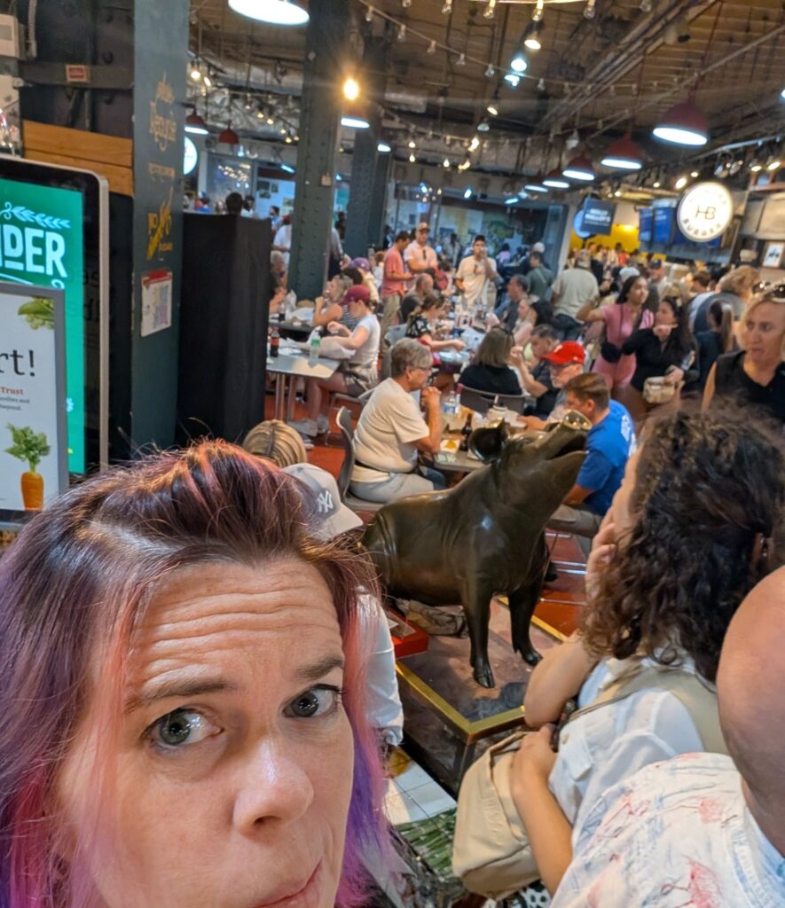 selfie of a person in a crowded corridor and a large bronze pig statue
