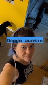 selfie of a person smiling with two dogs eating in the background and the text overlay that says Doggo auntie