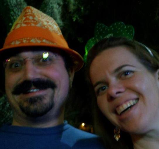 blurry selfie of two people smiling at the camera with one wearing a paper tiara and one wearing an orange and tan straw hat