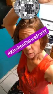selfie of a person dancing in a kitchen with a sticker overly of a disco ball and the hashtag for Kitchen Dance Party
