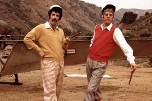 vintage phot of Eliot Gould and Donald Southerland in golfing attire on a set in scrubby California foothills