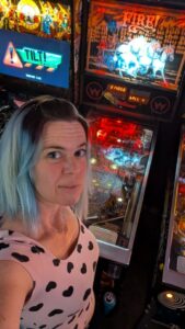 selfie of a person looking up from in front of a brightly lit pinball game with the word Fire above galloping horses