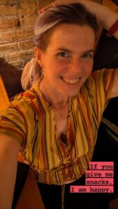 a selfie of a person in a yellow striped shirt and her hand on her head with the text 'If you give me snacks, I am happy."