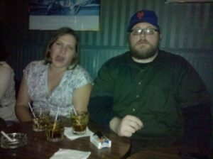 two people are sitting on a bench in a pub making faces at the camera