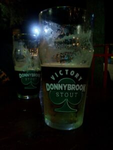 two glasses of beer in a dark area with logos for Victory Donnybrook Stout